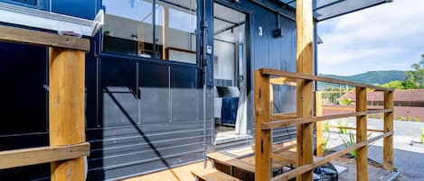 A modern building with a black exterior, wooden steps leading to a door, and a covered outdoor area.