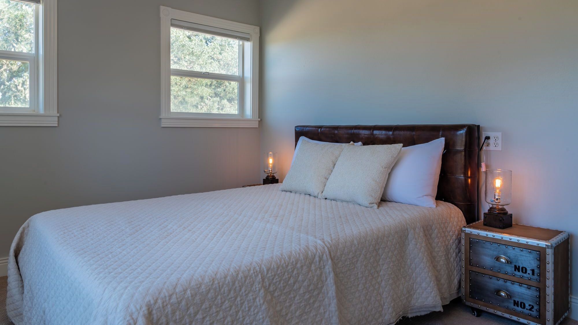 Un dormitorio con cama, dos lámparas de noche, una mesita de noche y un aparador con cajones.