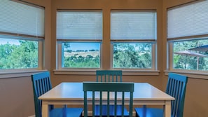 A dining area with a table and chairs, large windows with blinds, and a view of a green landscape. - Graceful Oaks by Avantstay Pool + Oak Trails + Lawn Games Near Paso Robles (Paso Robles)