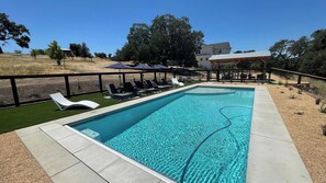 A rectangular swimming pool with clear blue water, surrounded by a black fence. There are several lounge chairs aligned along the poolside. - Graceful Oaks by Avantstay Pool + Oak Trails + Lawn Games Near Paso Robles (Paso Robles)