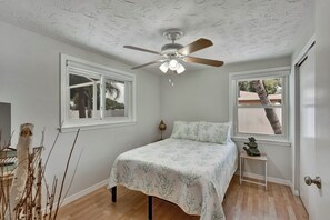 A bedroom with a bed, a ceiling fan, two windows, a nightstand, and a door. - Pool home 10 minutes to beaches.  Sleeps 6.  Outdoor Fireplace with grill grate. (Sarasota)