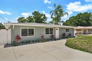 A single-story residential building with a light-colored exterior, a front porch, and a small front yard with decorative plants. - Pool home 10 minutes to beaches.  Sleeps 6.  Outdoor Fireplace with grill grate. (Sarasota)