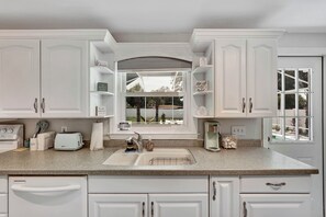 A kitchen with white cabinetry, a window with a view of palm trees, and a countertop with a toaster and a coffee maker. - Pool home 10 minutes to beaches.  Sleeps 6.  Outdoor Fireplace with grill grate. (Sarasota)
