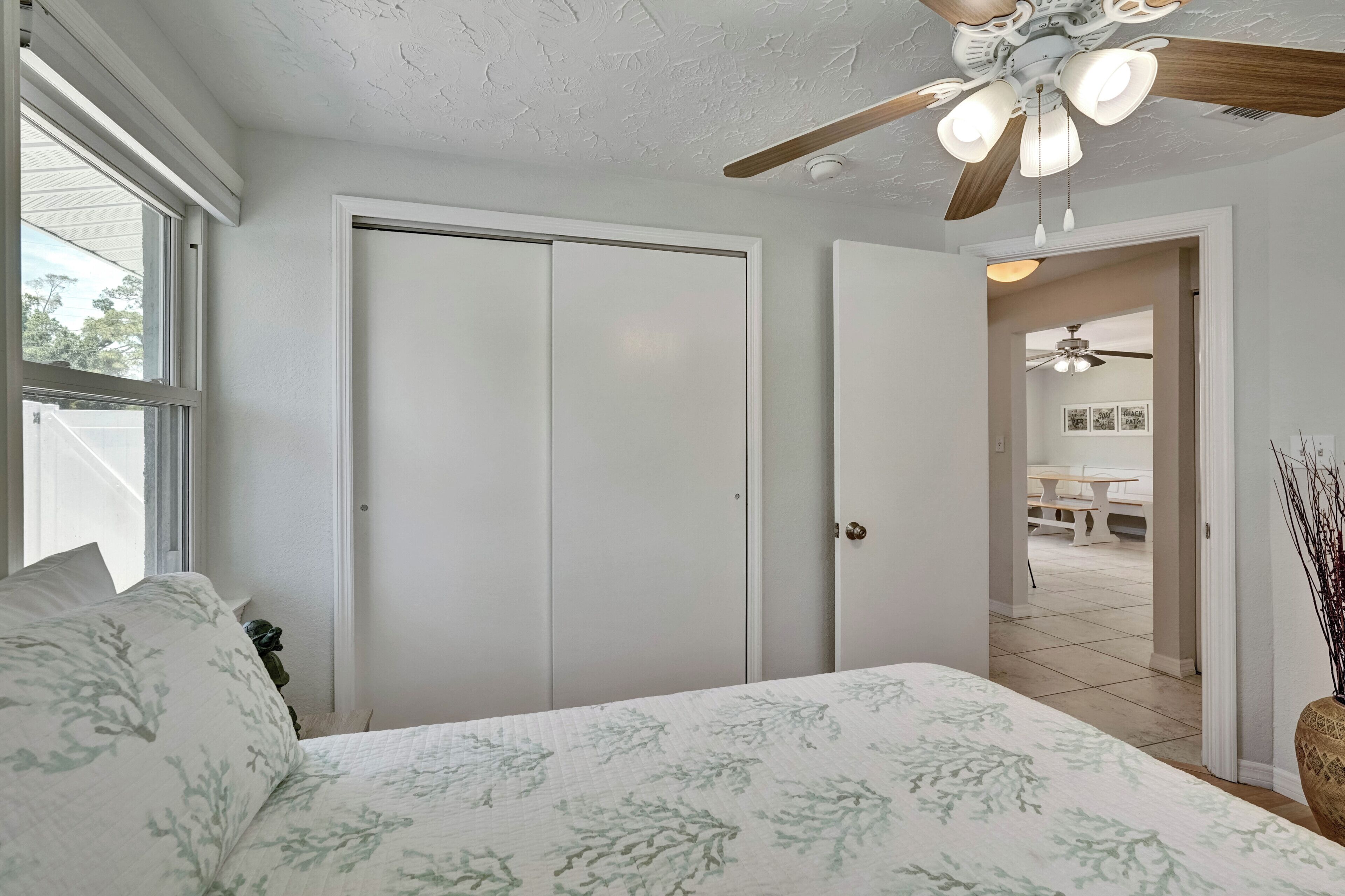 A bedroom with a bed, a ceiling fan, and a door leading to another room.