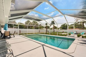 Piscina al aire libre techada con techo de vidrio, rodeada por una cerca blanca y equipada con sillas de descanso y una mesa.