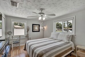Un dormitorio con cama, tocador con espejo, lámpara de pie y ventilador de techo.