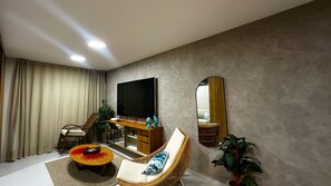 Una sala de estar moderna con un televisor de pantalla plana, un sofá, una silla, una mesa de centro y un espejo en la pared.