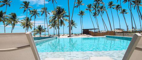 A pool with clear blue water, surrounded by palm trees and lounge chairs.