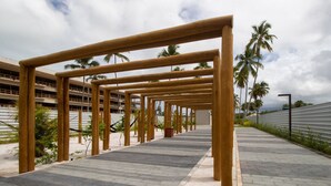 A pathway with wooden structures, palm trees, and a building in the background. - Beachfront Condos at Ipioca Beach Life Maceio by MME (Maceió)