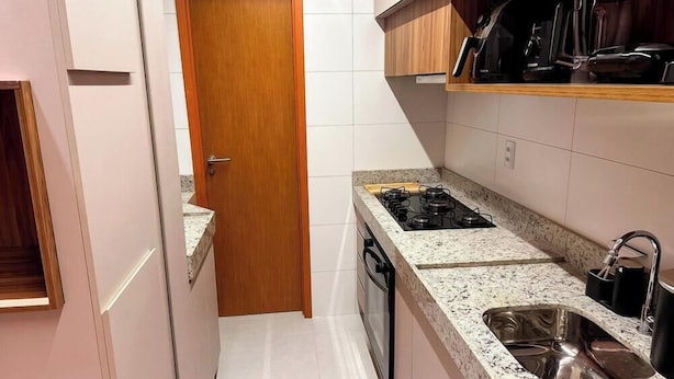 A compact kitchen with a gas stove, a sink, and wooden cabinets. - Beachfront Condos at Ipioca Beach Life Maceio by MME (Maceió)
