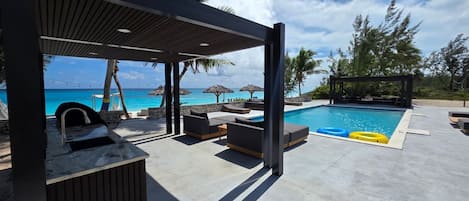 Zona de piscina con una zona de estar cubierta, una silla de descanso y vista al océano.