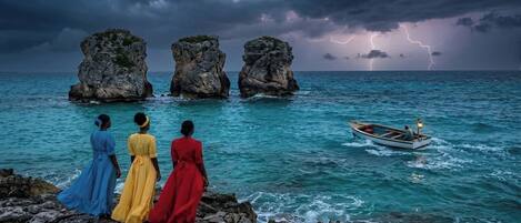 A rocky shoreline with three large rock formations and a boat in the water.