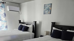 Hotellihuone, jossa on kaksi sänkyä, seinään asennettu ilmastointilaite ja taulu.
