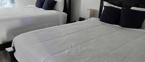 Et hotelværelse med to senge, en vægmonteret klimaanlæg og et billede.