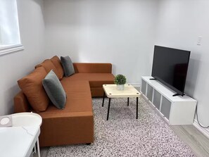 Een moderne woonkamer met een hoekbank, een bijzettafeltje, een potplant en een flatscreen televisie op een meubel.