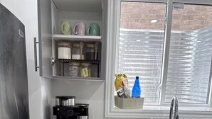 Une cuisine équipée d’un réfrigérateur en acier inoxydable, d’une machine à café, d’un grille-pain et d’une fenêtre donnant sur un mur de briques.