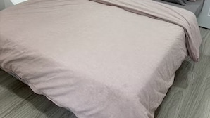 Un lit avec une couvre-lit à rayures et deux oreillers, dans une pièce dont le mur est gris et le sol en bois.