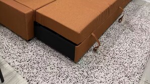 Un canapé modulable doté d’un compartiment de rangement, placé dans un coin, avec un tapis à motifs et une fenêtre.