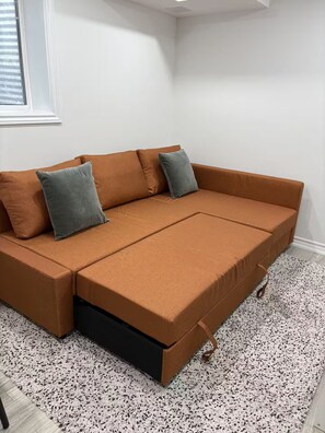 A sectional sofa with a storage compartment, positioned in a corner with a patterned rug and a window.