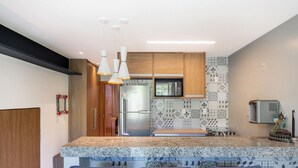 A modern kitchen with granite countertops, stainless steel appliances, and a decorative Buddha statue. - Beautiful Apartment Near the Beach Sov0005 (Mata de São João)