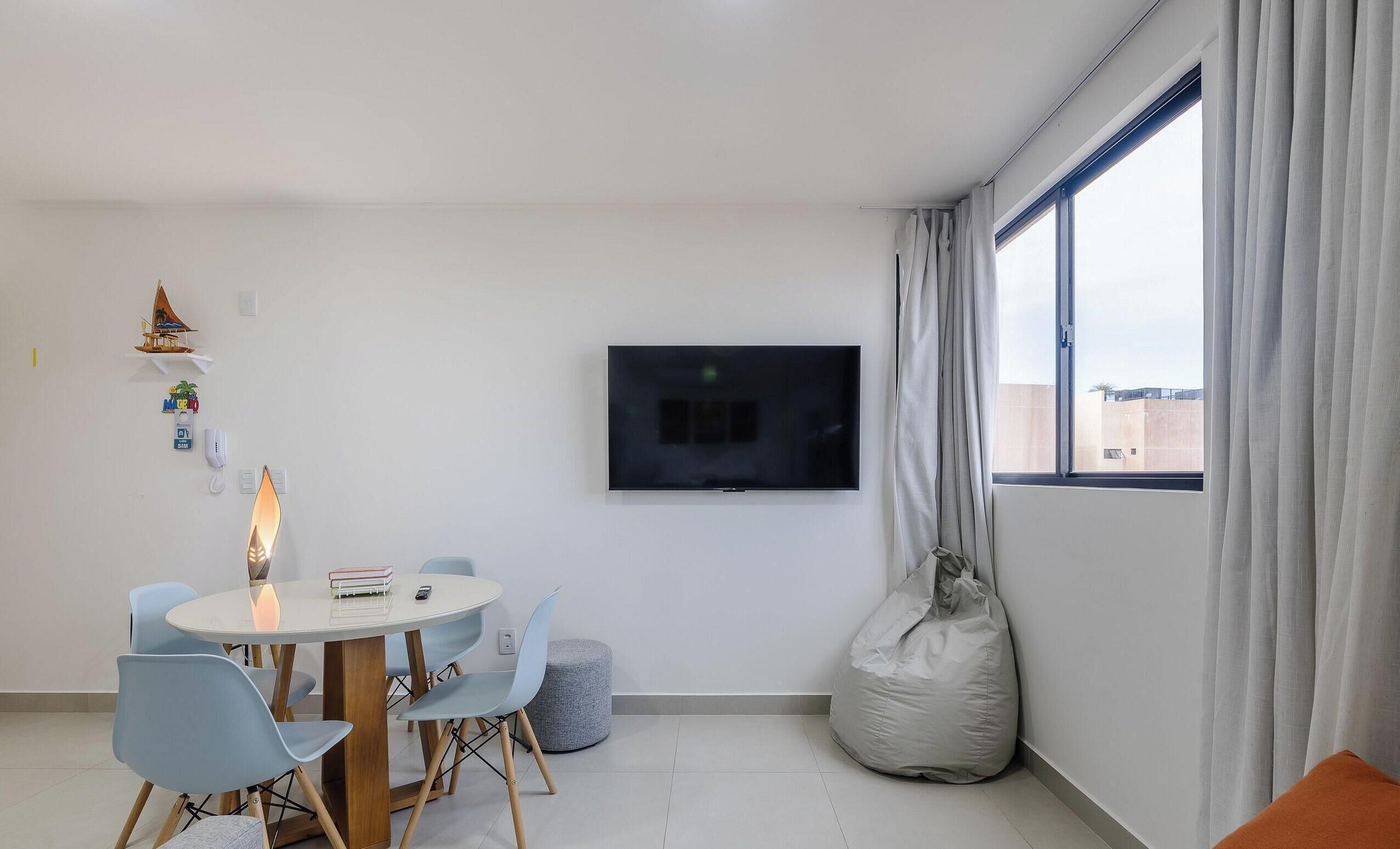 Una sala de estar moderna con una mesa redonda, sillas, un televisor y un ventanal con cortinas.