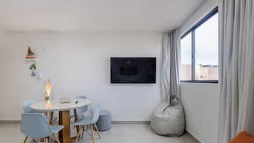Una sala de estar moderna con una mesa redonda, sillas, un televisor y un ventanal con cortinas.