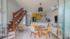 Cuina moderna amb una illa central, cadires grogues i una escala de fusta.