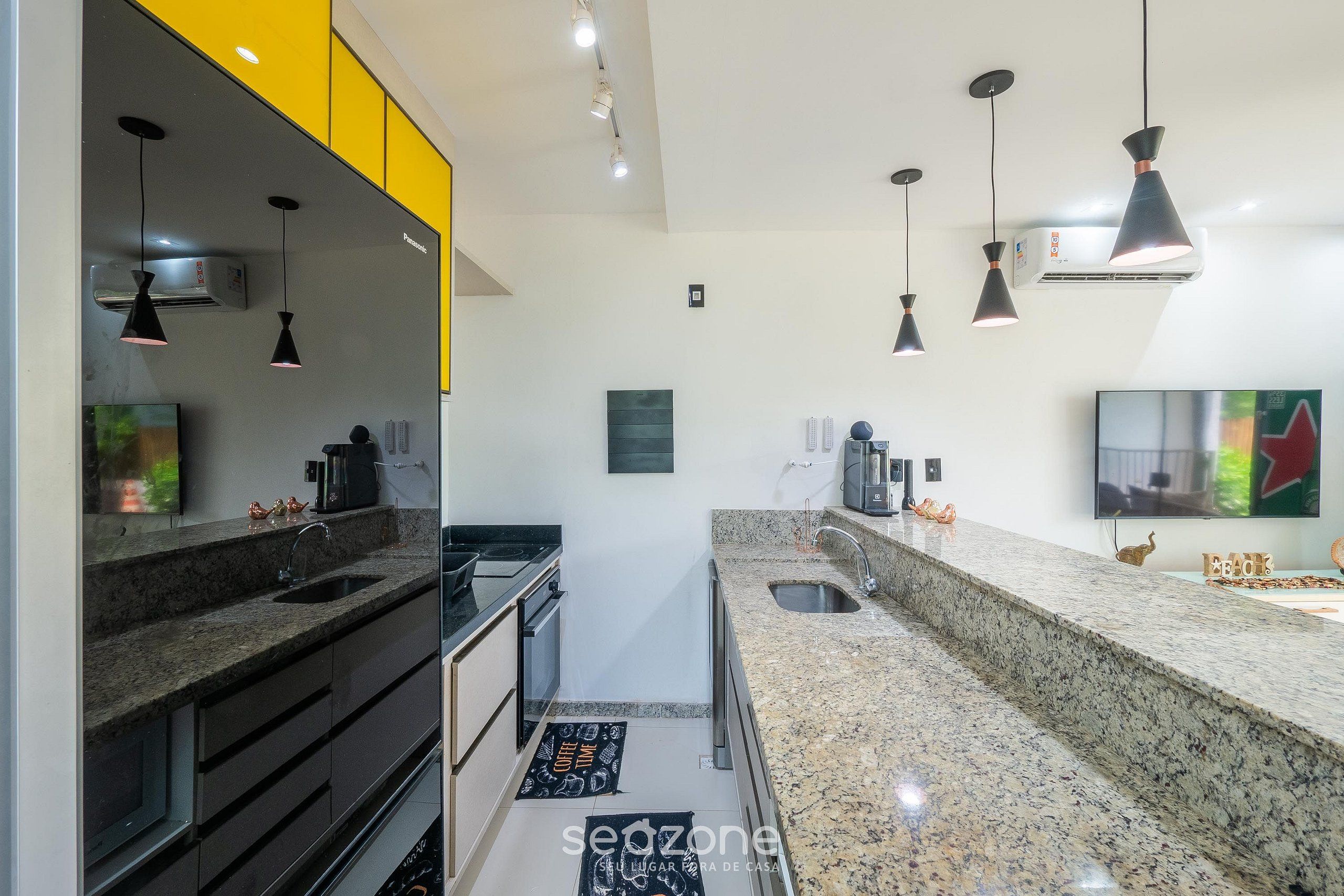 Una cocina moderna con encimeras de granito, armarios negros y amarillos, e iluminación colgante.