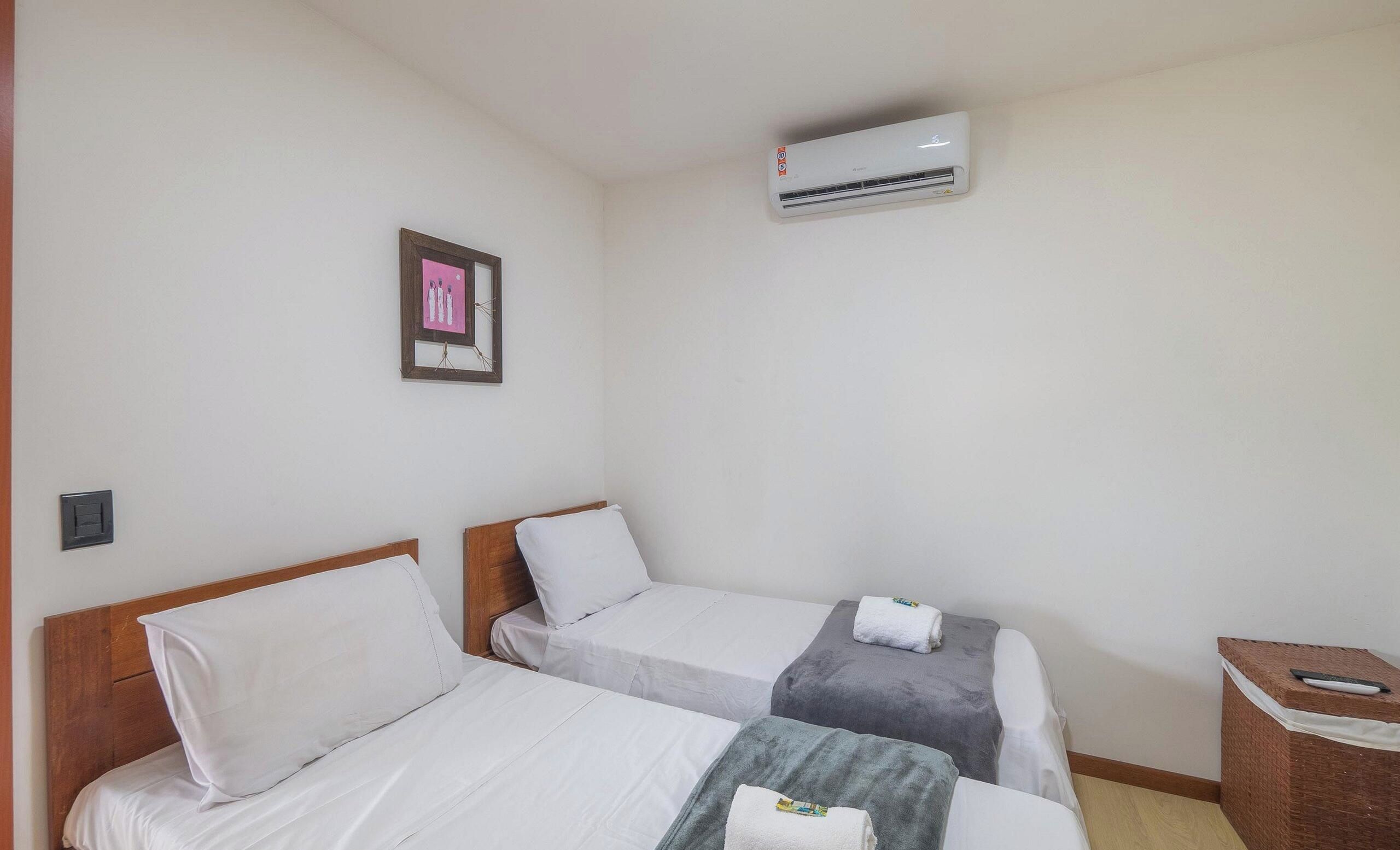 A hotel room with two beds, a wall-mounted air conditioner, and a framed picture.