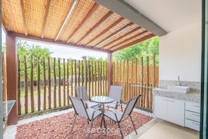 Eine Terrasse mit einem Glastisch und Stühlen, einem Holzzaun und einer Küchenzeile mit Spüle.