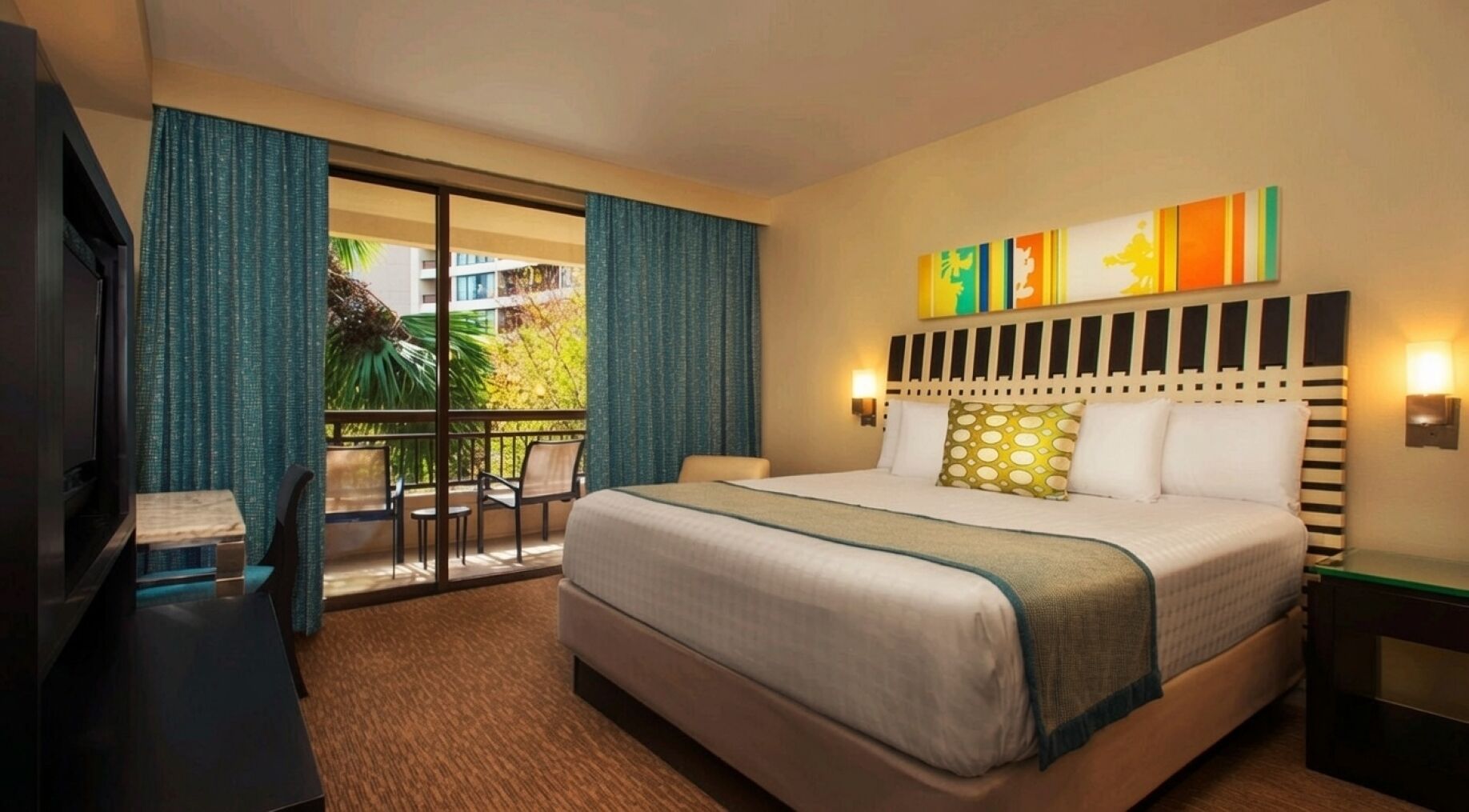 A hotel room with a bed, a television, a balcony with chairs, and a view of the outside.