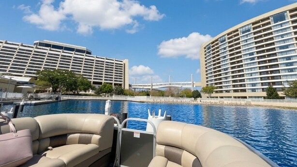 Um barco com assentos e vista para a piscina de um hotel com vários andares e uma ponte ao fundo.