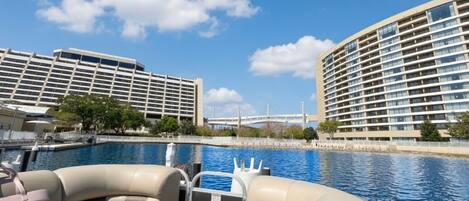 Un bote con asientos y vista a una piscina, con un hotel de varios pisos y un puente al fondo.