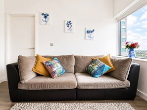 A living room with a beige sofa, two patterned throw pillows, a white rug, and three wall-mounted floral artwork. - Spacious 2BR Sleeps 7, Long Stays (Croydon)