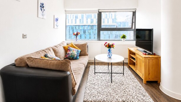 Ein modernes Wohnzimmer mit einer Couch, einem Couchtisch, einem Fernseher und einem Fenster mit Blick auf die Stadt.