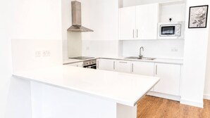 Eine moderne Küche mit weißen Schränken, einer Edelstahl-Dunstabzugshaube, einer eingebauten Mikrowelle und Holzboden.