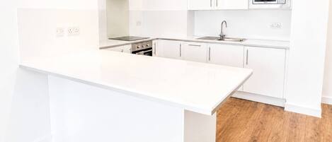 A modern kitchen with white cabinetry, a stainless steel range hood, a built-in microwave, and a wooden floor.