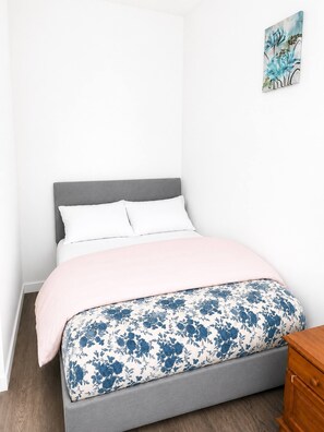 Ein Bett mit grauem Kopfteil, weißen Kissen, einer pinken Decke und einer Bettdecke mit Blumenmuster.