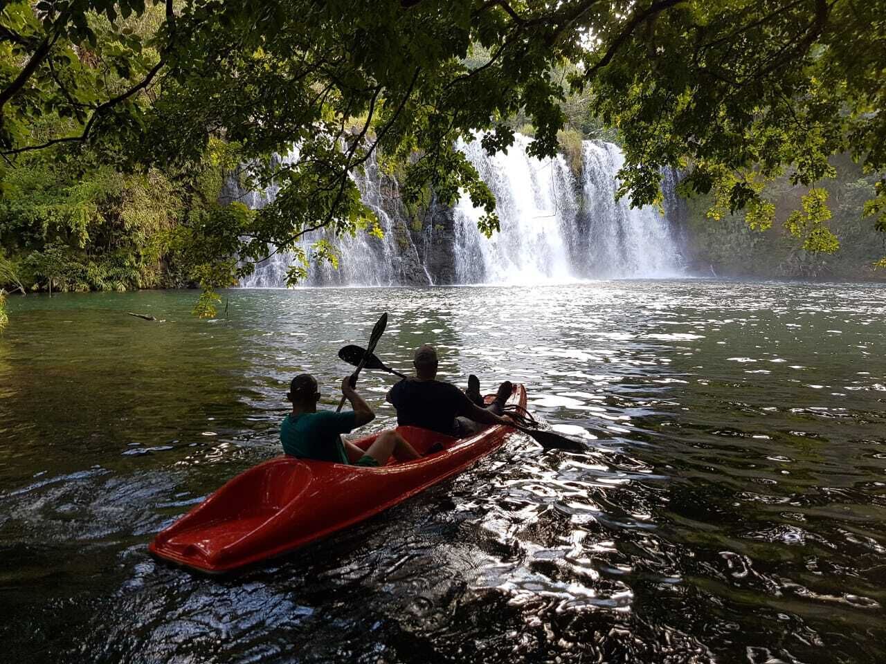 A red canoe on a calm river with a waterfall in the background.