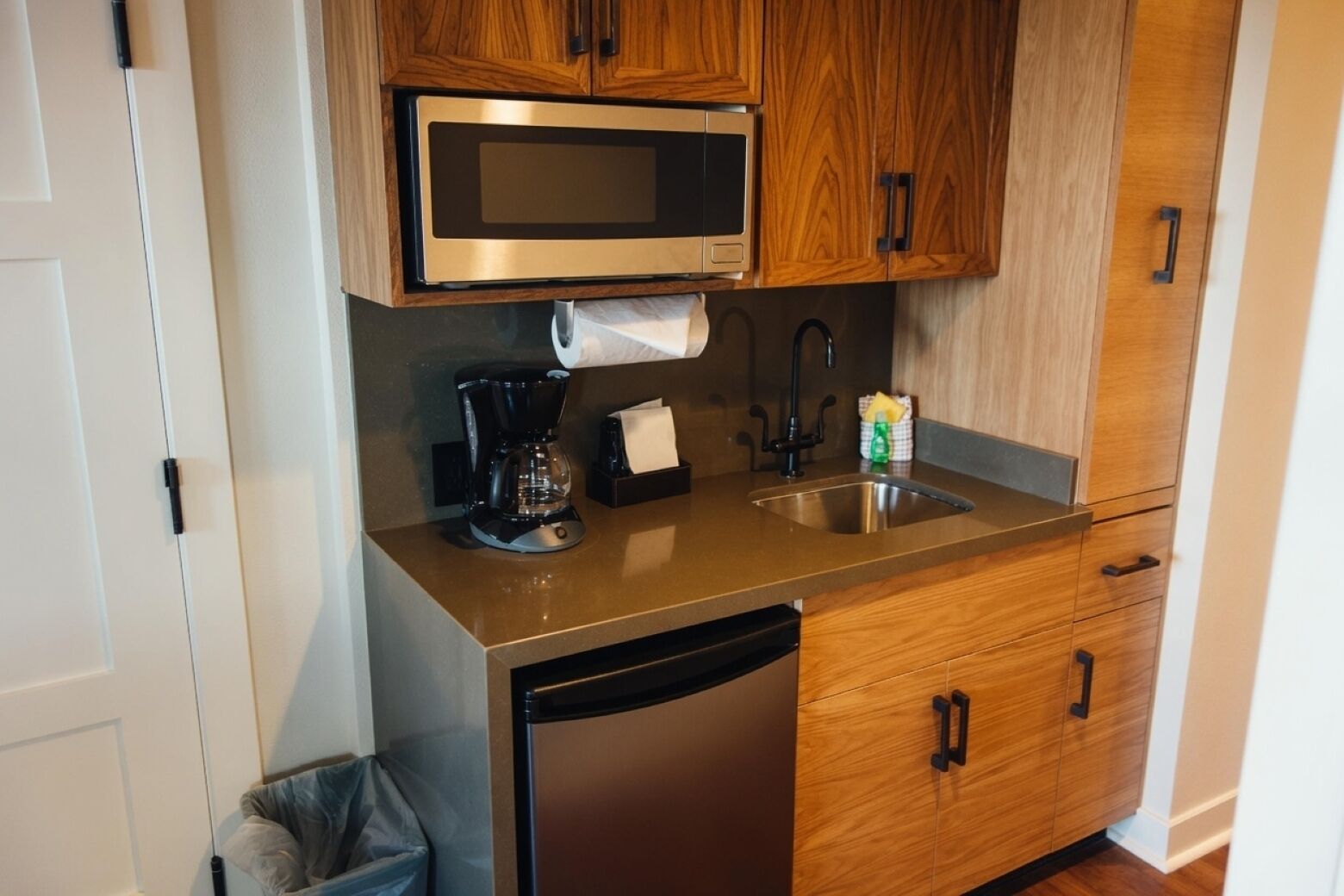A compact kitchen with a microwave, coffee maker, sink, and wooden cabinets.