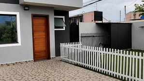 Een modern gebouw met twee verdiepingen, een betegeld terras, een houten deur en een witte hek.'