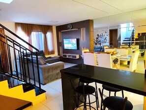 A modern living room with a sofa, a TV, a staircase, and a dining area with chairs.