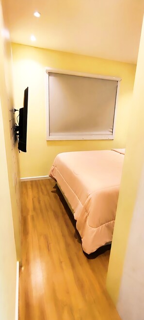 A narrow room with a bed, a mounted television, and a window with blinds. - JKLL INN 1980 HOME FULL 15 min from CWB Airport / 5 min from the Botanical Garden  (Curitiba)