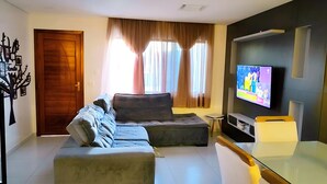 Een moderne woonkamer met een modulaire bank, een glazen salontafel, een flatscreen televisie en een deur met een decoratief kunstwerk.