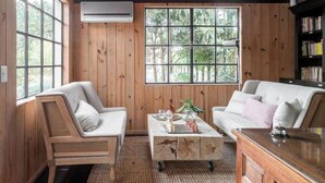 A room with wooden walls, a large window, a sofa, a chair, and a coffee table.