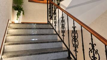 A marble staircase with ornate black railings and a wooden handrail, leading to a landing with a framed artwork and a potted plant.