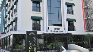 Un edificio de hotel con un gran ventanal arqueado, varios balcones con toldos verdes y un letrero que dice 'Janset Boutique Hotel'.