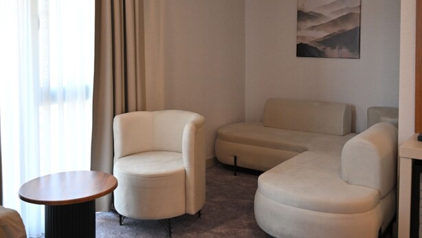 Una habitación de hotel moderna con un ventanal grande, una mesa de centro redonda, dos sofás y un cuadro en la pared.
