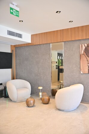 Un espace d’attente moderne, doté de deux fauteuils confortables, d’une table basse en verre et d’un miroir décoratif qui reflète la pièce.