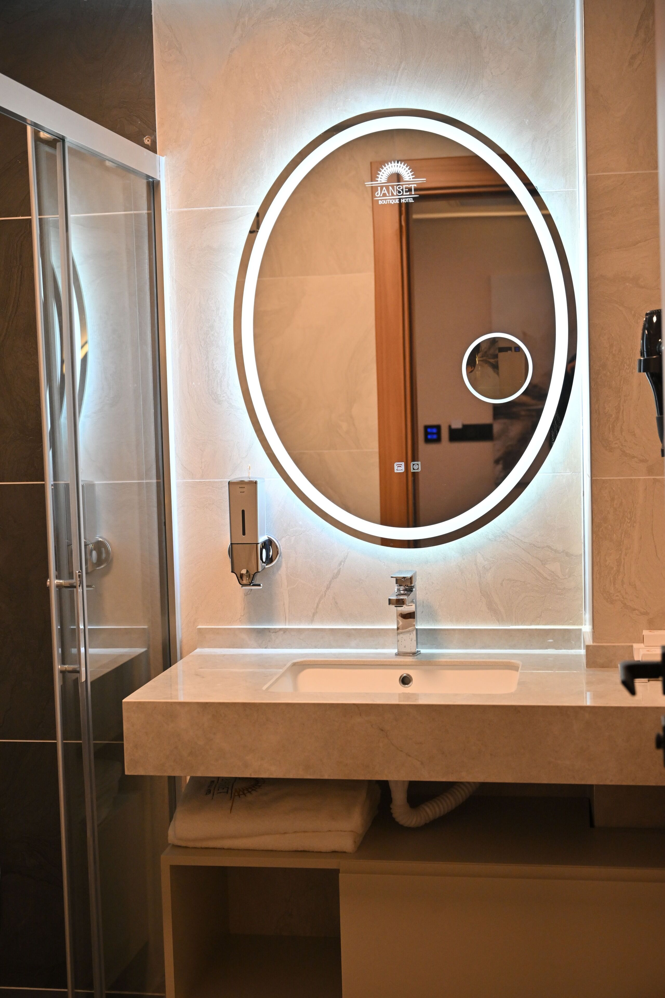 Un baño con tocador moderno, un espejo redondo con iluminación perimetral y cabina de ducha de vidrio.